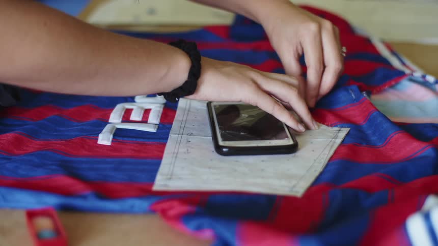 A woman holds a pattern atop a sports jersey and makes marks on it for alterations