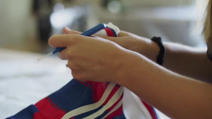 A woman using a blue seam ripper to open the seam on a shirt