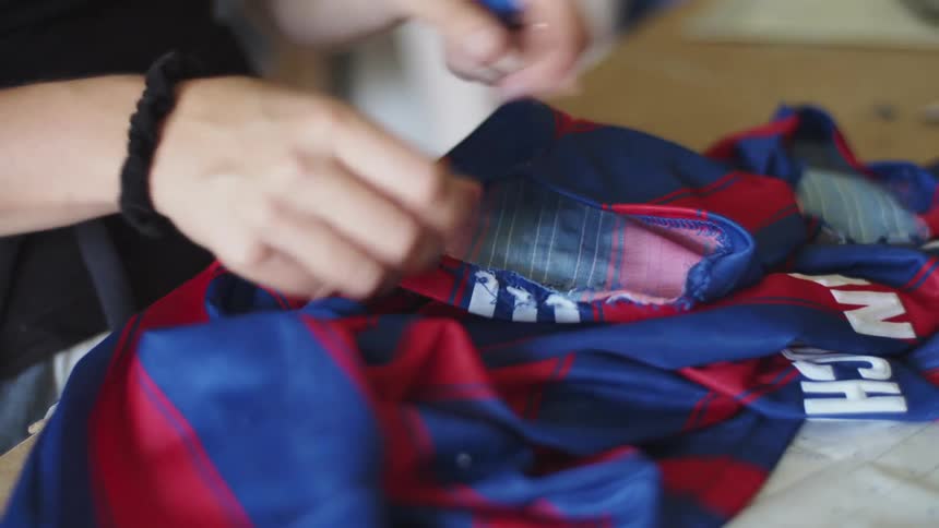 A woman stands at a table and uses a tool to remove a seam from a shirt