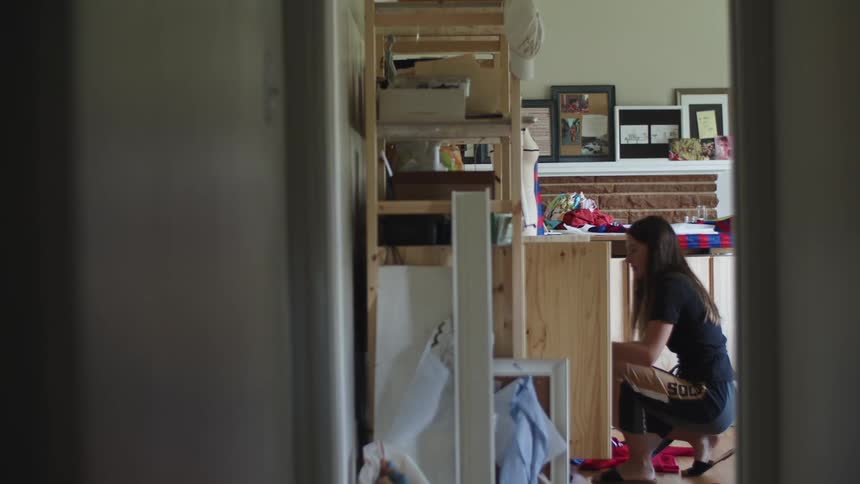 Woman squats down in front of a wooden cabinet and starts taking clothing out of it inside of a room in a house