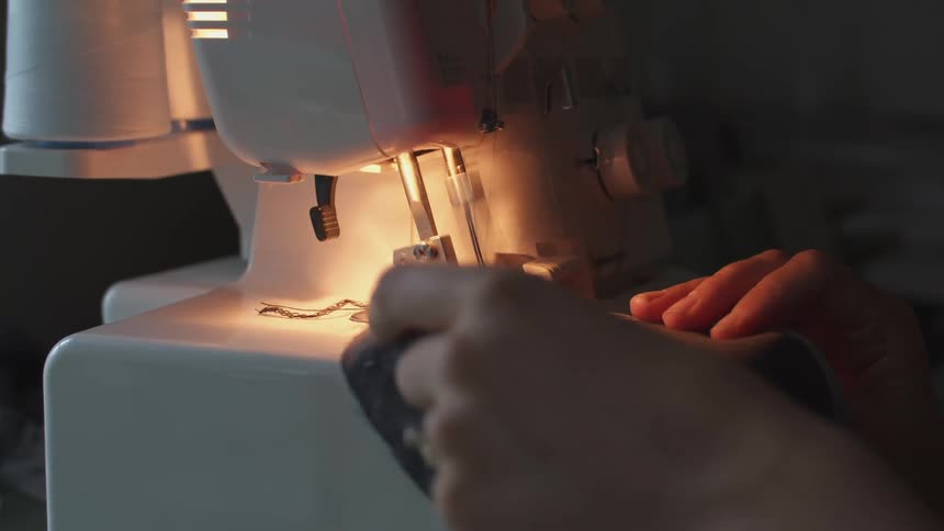 Woman running a piece of grey fabric under a moving needle through a sewing machine