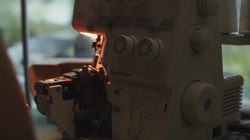Woman threading a sewing machine in a dimly lit room