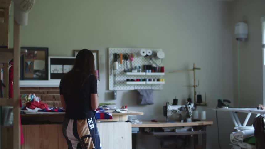 Woman works at a table covered with cloth in a craft room filled with sewing tools