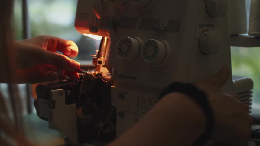 Woman putting a piece of thread into a sewing machine with its light on