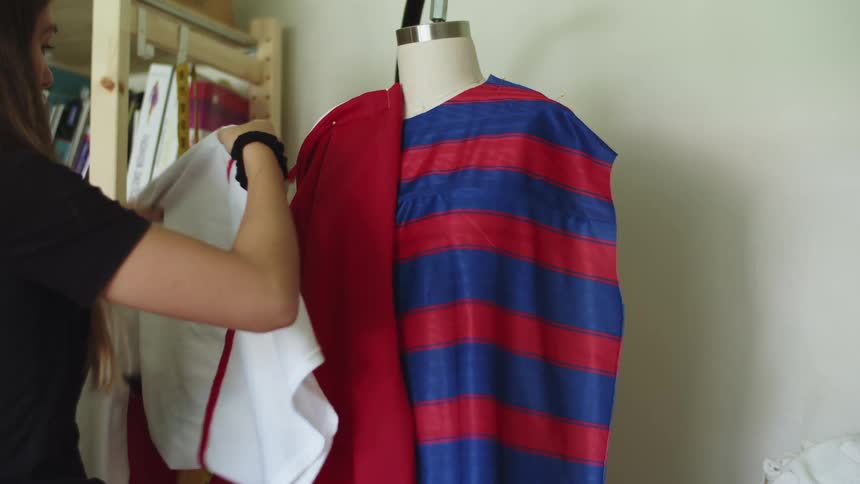 A woman drapes fabric on a dress form in a room during the day