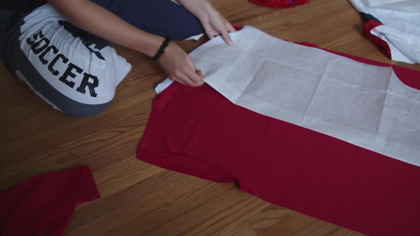 A woman lays fabric down on the floor and places a pattern ontop