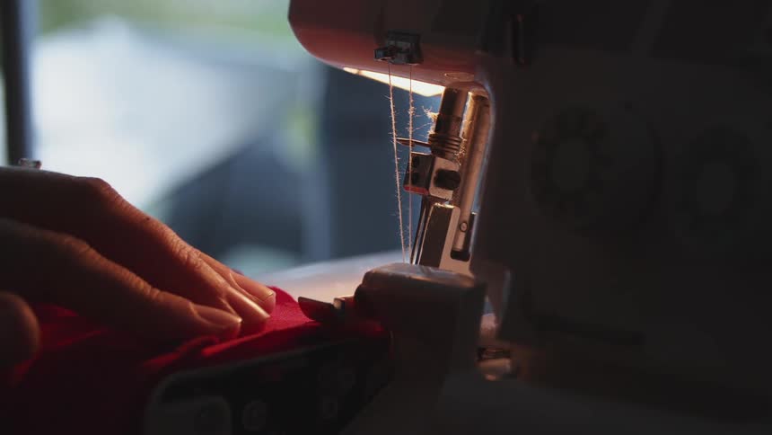 Woman stitching clothing on a sewing machine in a dimly lit room at home