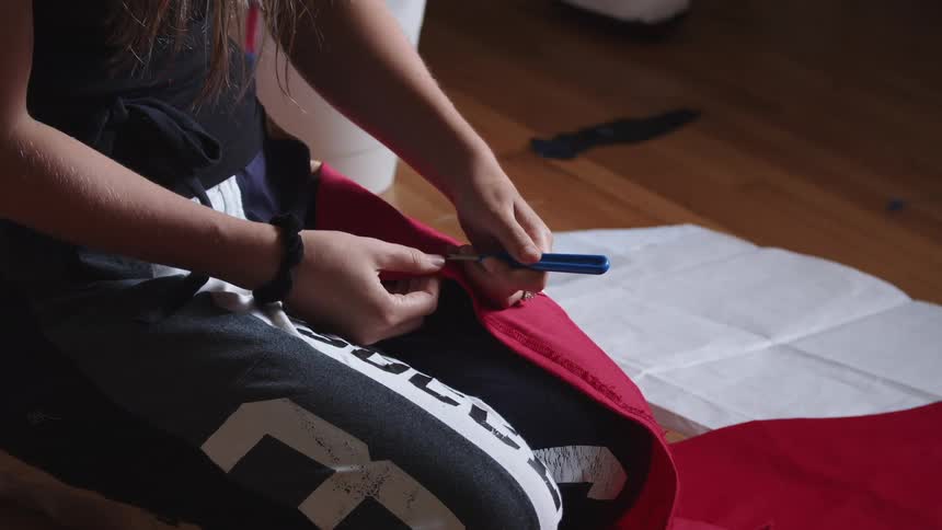 Woman sits on hardwood floor and pulls stitches from red cloth