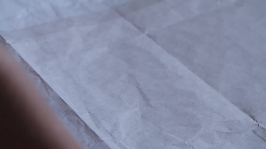 A person places and removes a piece of white paper over red fabric on a flat surface