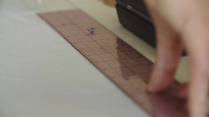 A man uses a ruler to draw a straight line on a piece of paper