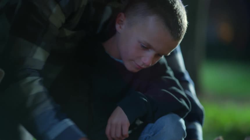 Boy learning from his father how to start a campfire with flint and steel