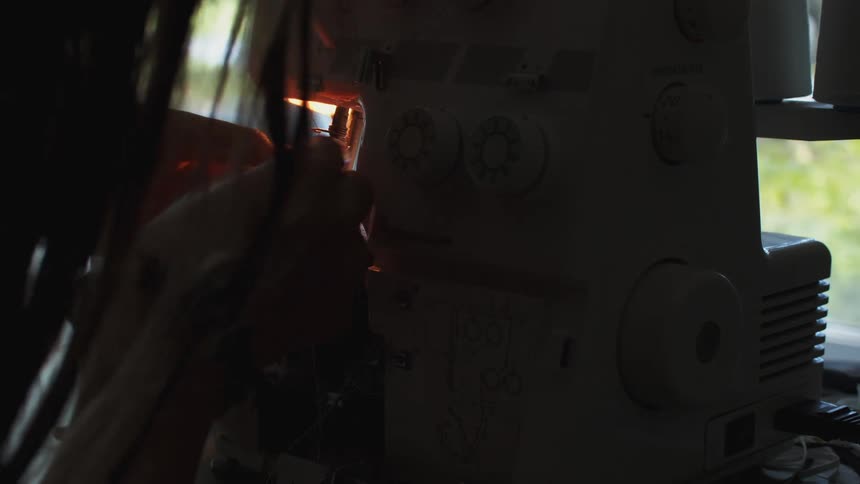 Woman reaching into a sewing machine with a crochet hook adjusting the parts inside