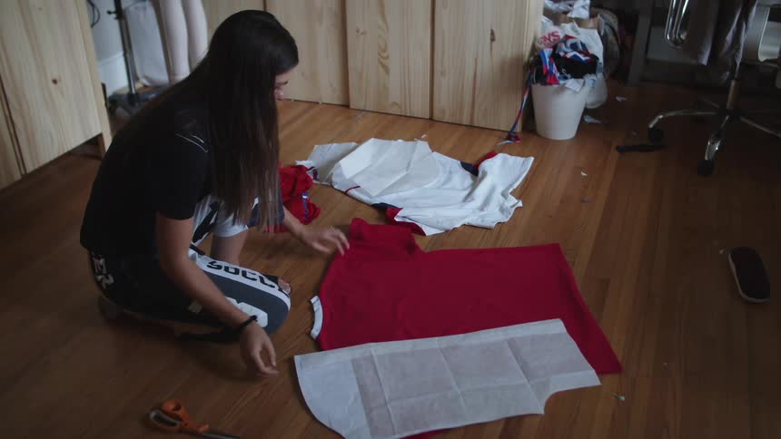 Woman kneeling on one knee taking measurements of a red shirt on a hardwood floor in a room