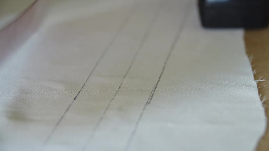 A person uses a ruler in order to draw parallel lines on a piece of fabric