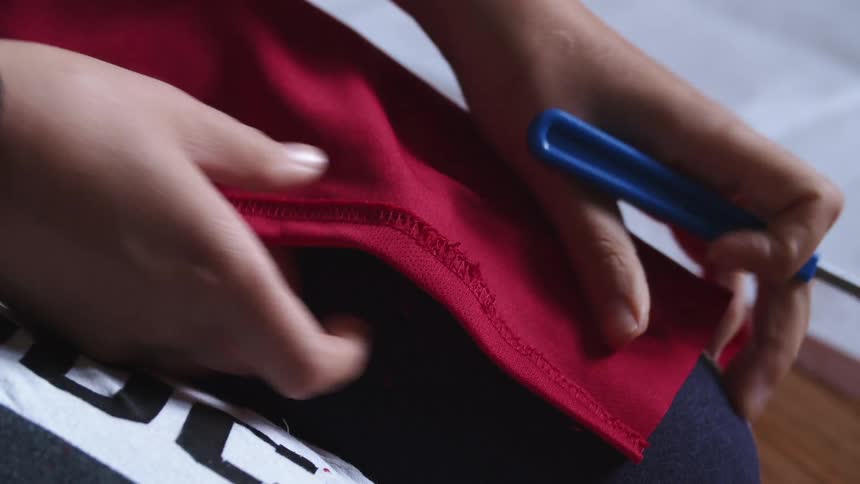 Taylor uses a seam ripper on the stitches of a piece of red cloth