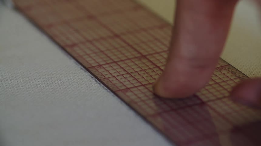 Hands taking measurements on a piece of fabric with a pen