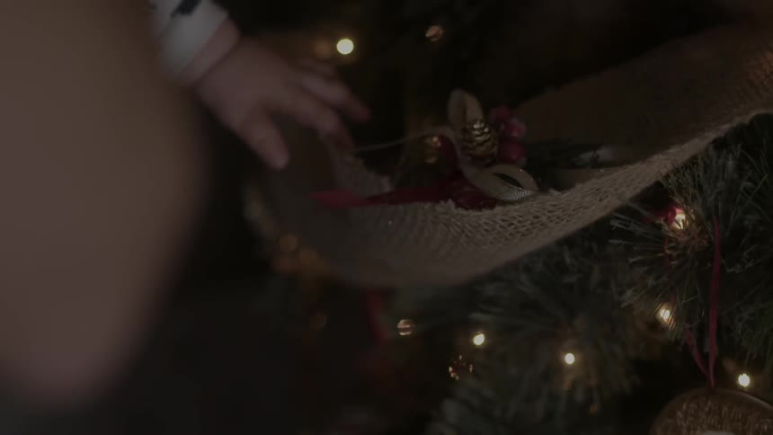 A baby reaches out and touches ornaments on a christmas tree