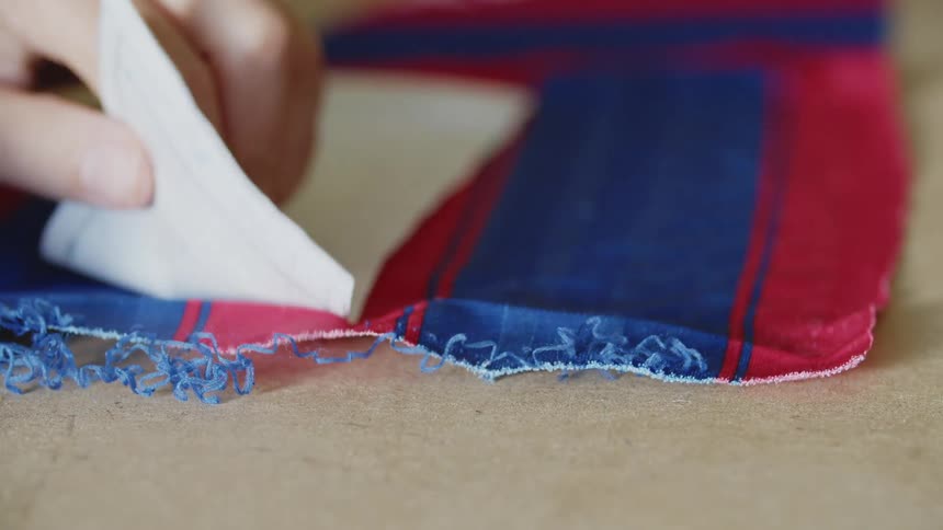 Hands using a piece of paper to take measurements on a piece of red and blue fabric
