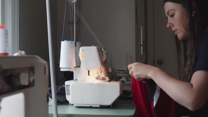 Woman sitting down readies a red black and white shirt in front of a sewing machine and places it in position to sew