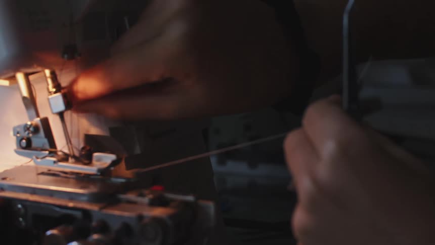 A person uses pliers to thread a sweing machine in a dimly lit room
