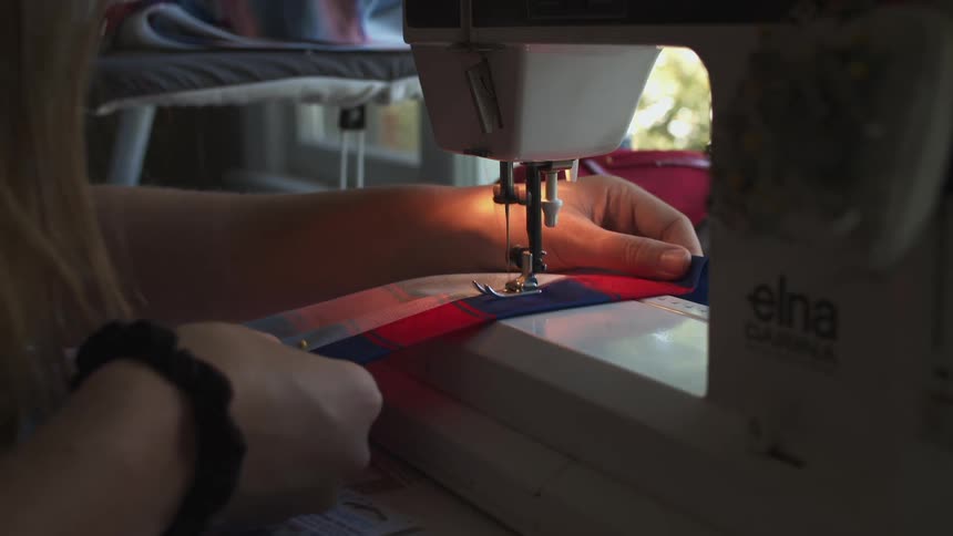 A woman uses a sewing machine on a piece of fabric indoors