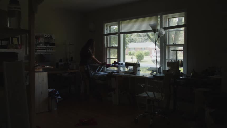 Woman ironing clothes on the ironing table next to the sewing machine in a room at home