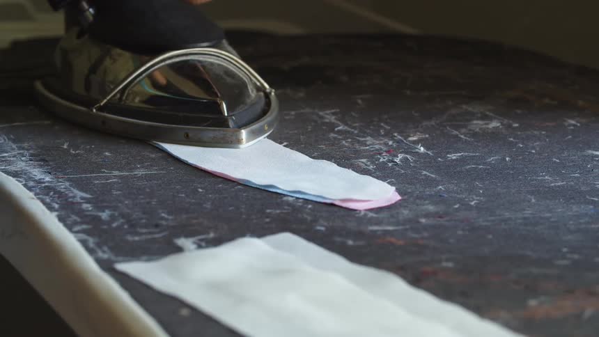 Person uses iron to press fabric flat on a black table