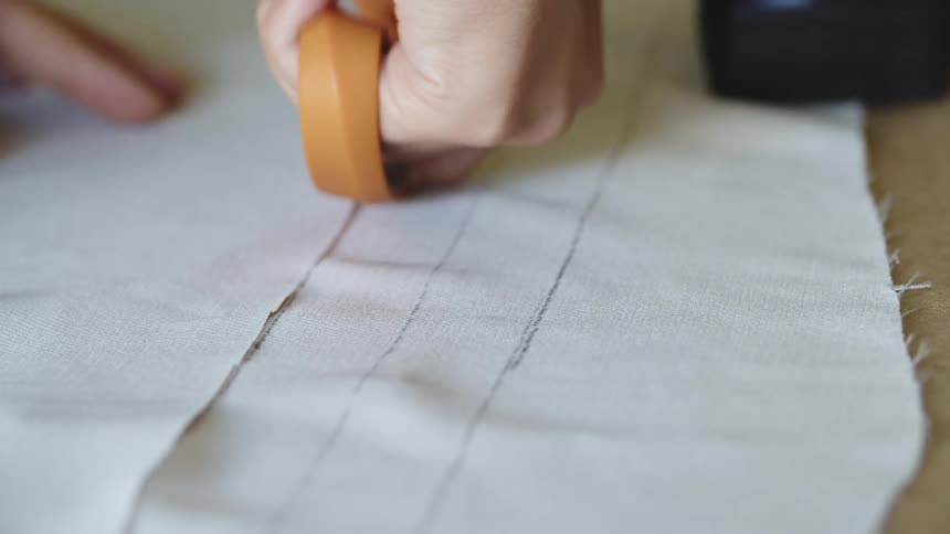 A taylor cutting a strips of clothing with scissors over a table