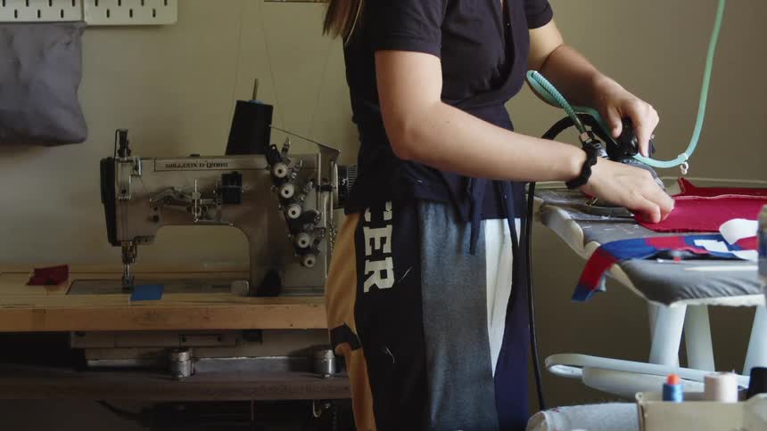 Young woman ironing clothes on an ironing table next to a sewing machine at home