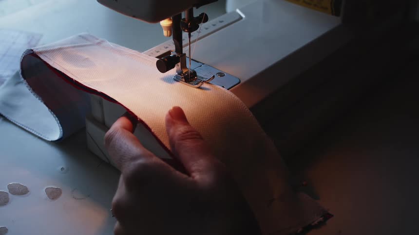 Tailor uses a sewing machine to stitch a piece of cloth in a dimly lit room