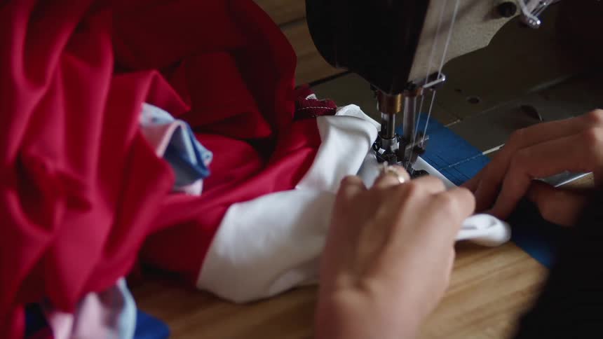 A woman stitching a piece of white and red fabric with a sewing machine