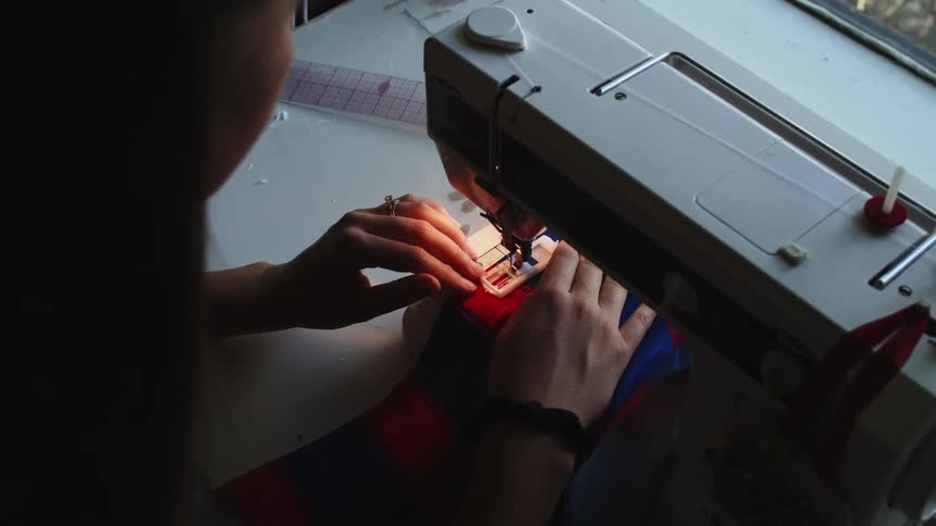 A woman sits at a sewing machine pushing fabric in line to stitch
