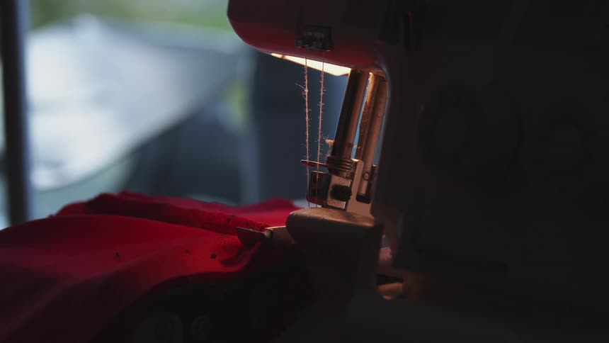A woman guides red fabric through a sewing machine that is sitting in front of her