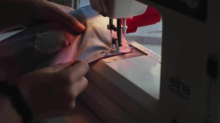 Taylor stitching a piece of cloth in a sewing machine at home