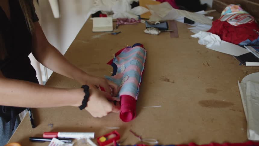 A woman stands at a table rolling fabric and pinning it for sewing indoors