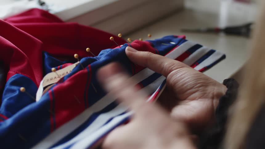 A woman sits at a table holding fabric adjusting pins in place to sew