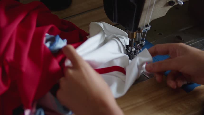 Womans hands using a sewing machine on a table to sew together a red and white shirt