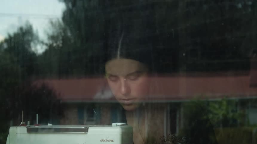 Woman looking down behind a window in front of a white sewing machine