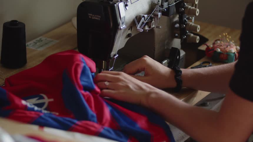 A woman carefully operates a sewing machine to sew a piece of red and blue fabric