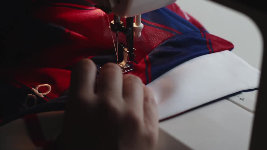A woman stitching a piece of red and blue fabric with a sewing machine