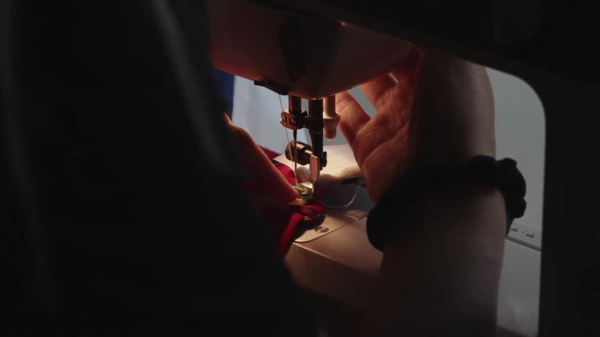 Tailor sewing a piece of cloth on a sewing machine in a dimly lit room