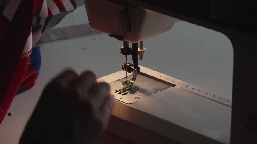A persons hands preparing material and a sewing machine to sew