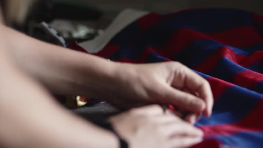 A woman pins the edge of a large piece of red and blue fabric to prepare it for sewing