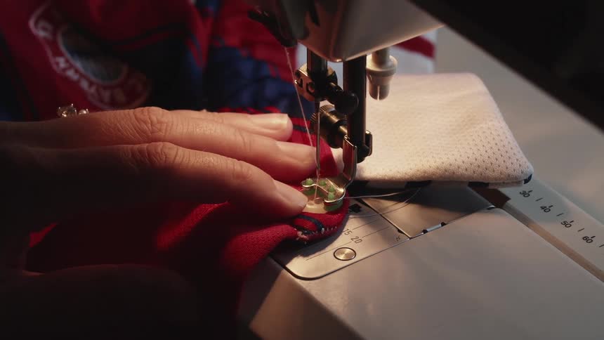 Sewing machine stitching a button onto the edge of a shirt