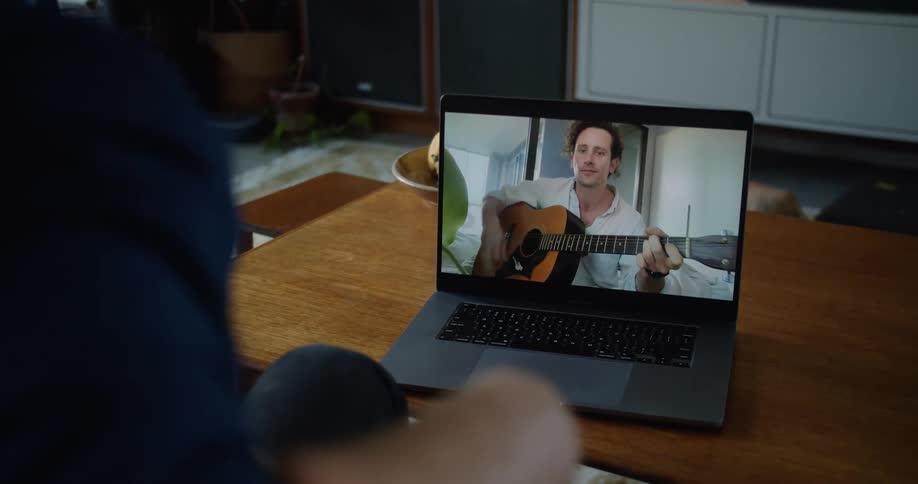 Man makes a video call with a man playing a guitar on his laptop