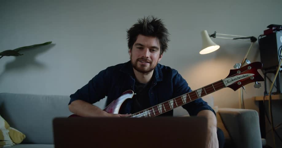 Young man holding a guitar while sitting on a couch in a video call on a laptop