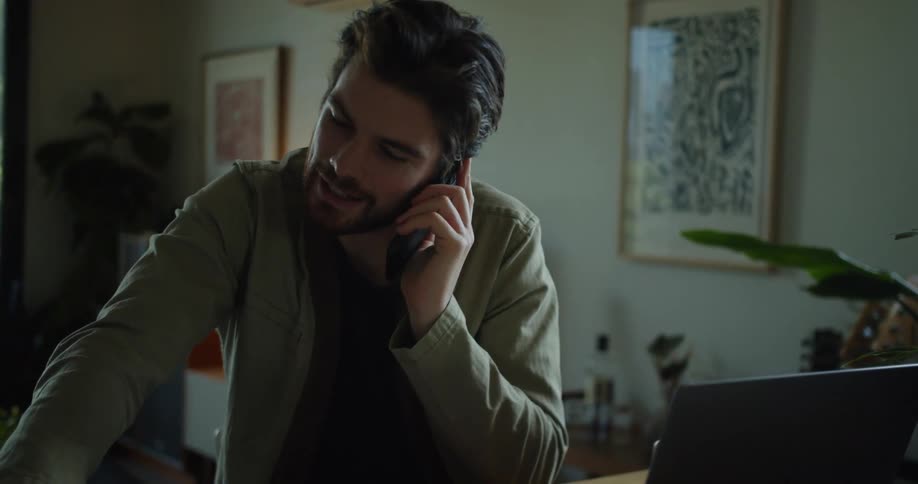 Man talks on the phone while pointing to a paper in a binder on a desk with a pen and an open laptop