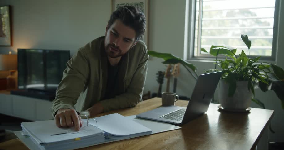Teacher giving an online class on a laptop checks information in a binder