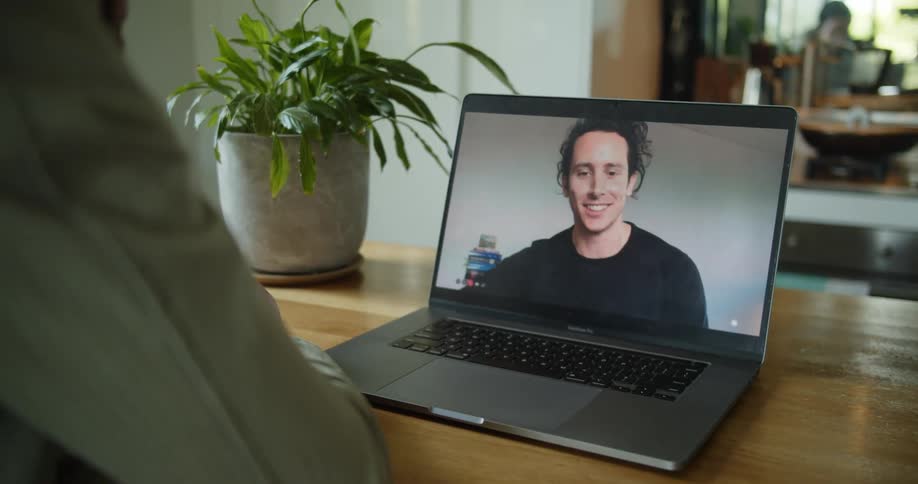 A man sitting at a desk participates in a video conference with another man using his laptop