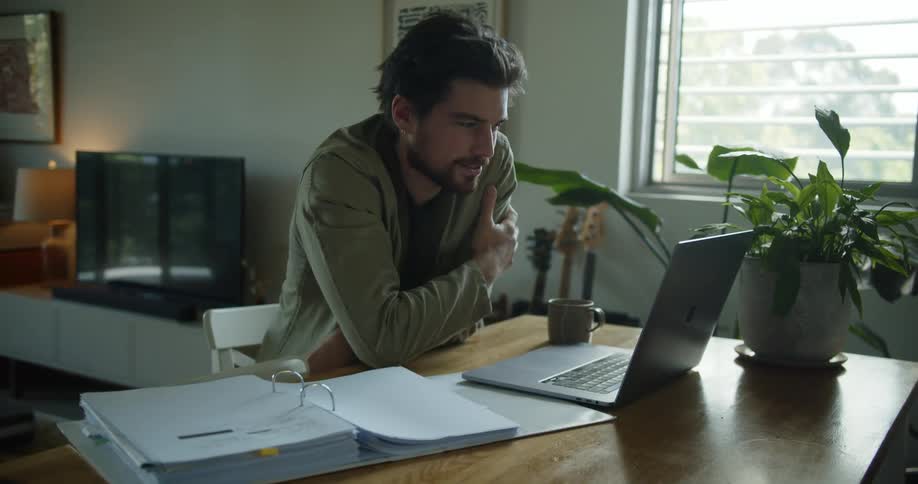 A person in a room sitting at a desk in front of a laptop